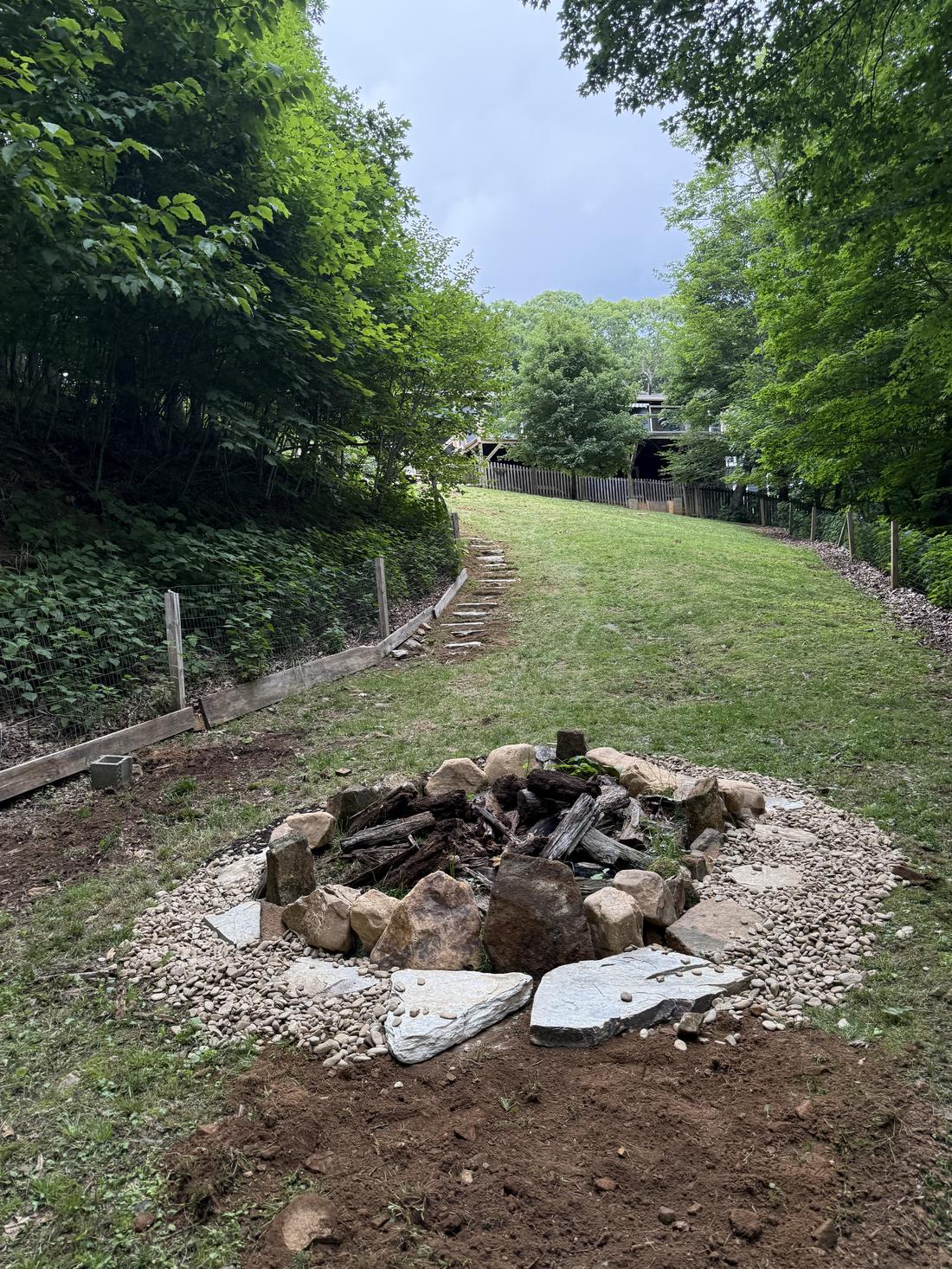 Stone fire pit with a river rock apron, set at the base of a graded and seeded lawn