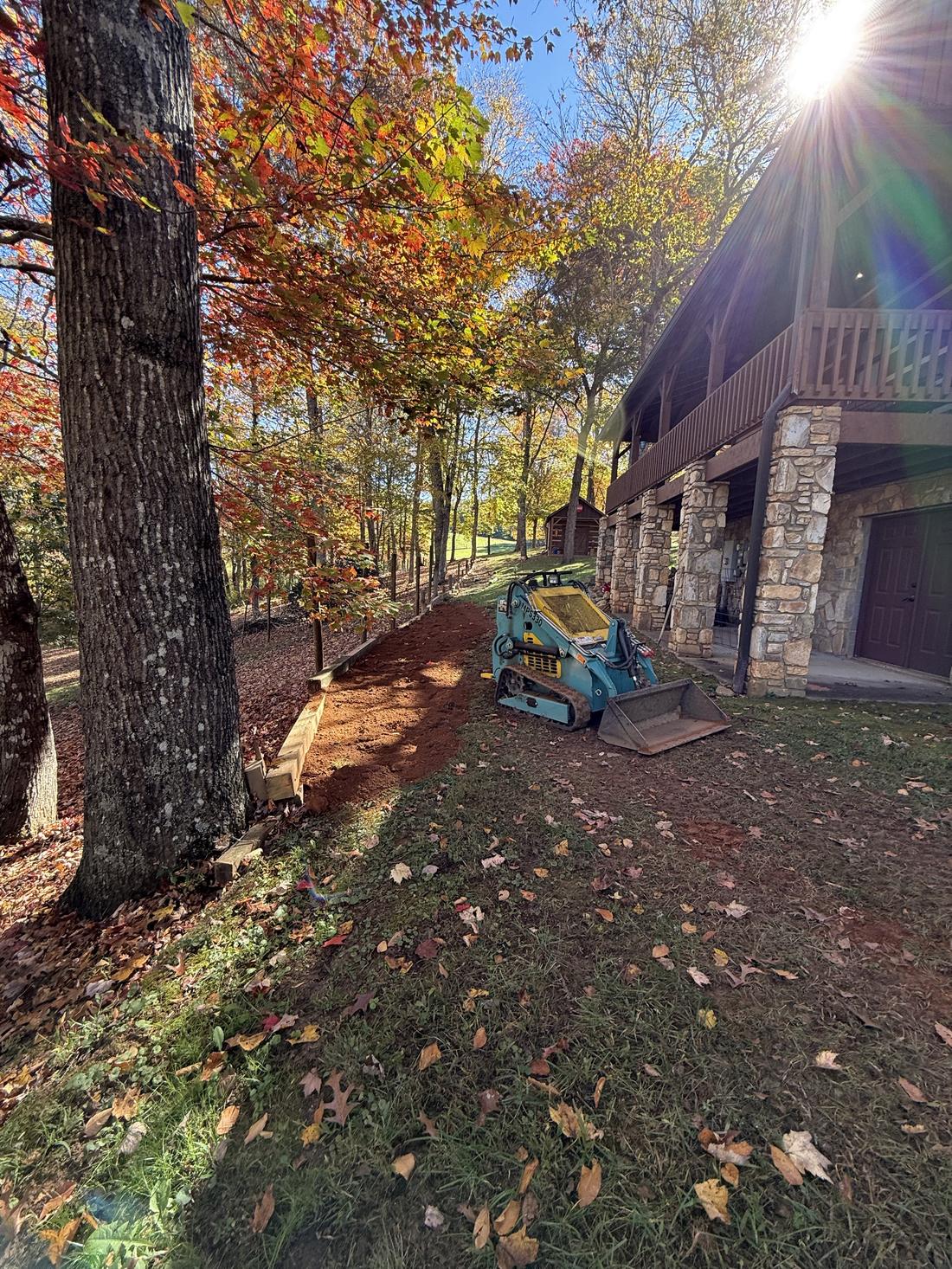 Compact track loader beside a house, with a new timber retaining edge and fresh clay along a slope